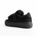 Zapatilla negra con pompón sobre fondo blanco